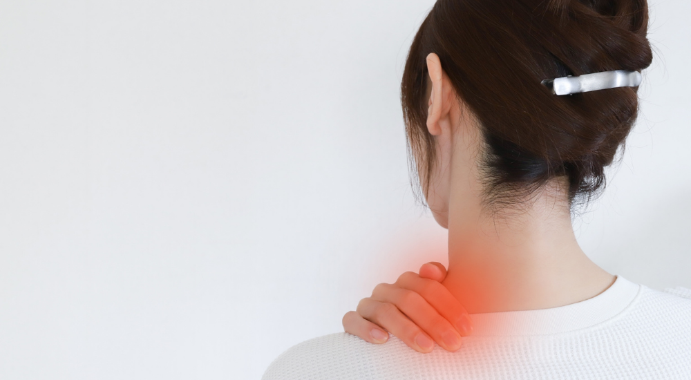 女性の後ろ姿で、【首の付け根から肩(僧帽筋上部付近)】が赤くハイライトされており、強い肩こりや炎症の痛みを抱えている様子。