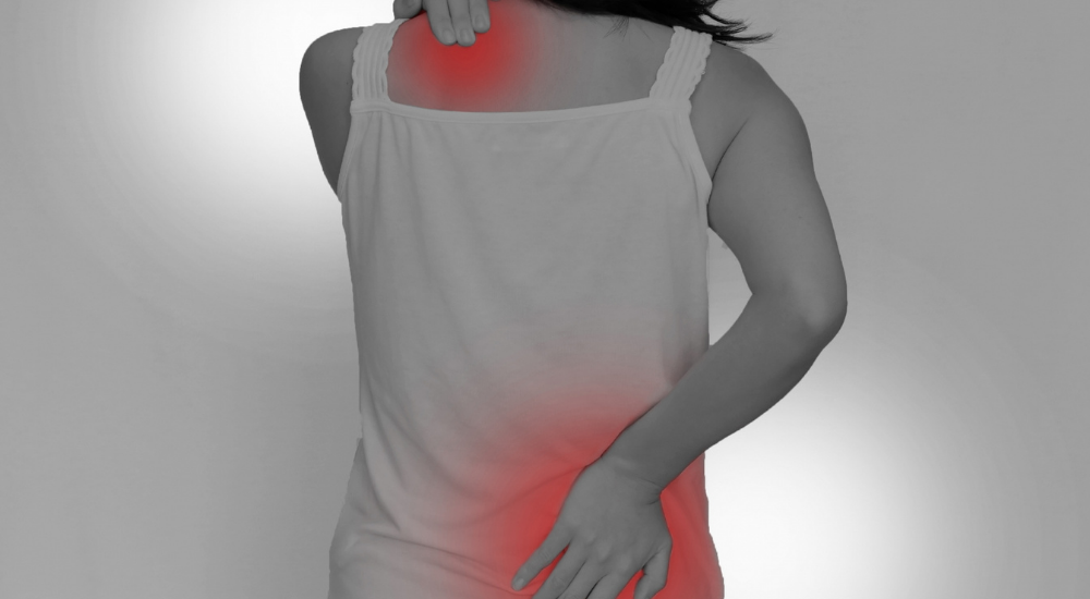 【左肩（僧帽筋）】と【右腰（腰方形筋・脊柱起立筋）】が赤くハイライトされ、肩こりと腰痛という複数の不調を同時に抱えて悩んでいる女性の後ろ姿。症状を強調させている画像。